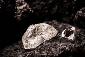 diamante bruto encima de rocas con un diamante pulido al lado